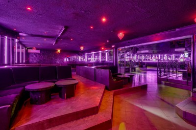 Intérieur d'une discothèque avec éclairage violet, escalier central, balustrades métalliques et sol carrelé coloré.