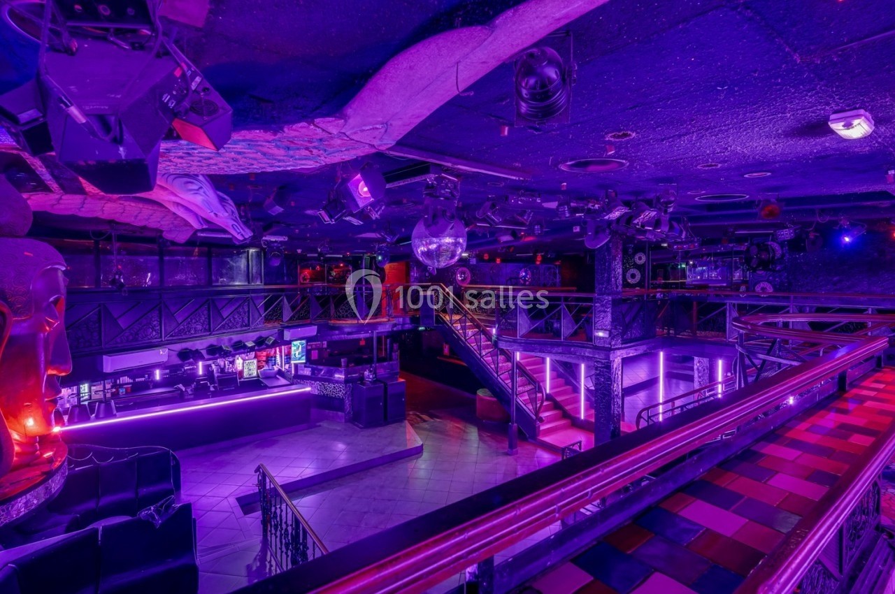 Intérieur d'une discothèque avec éclairage violet, piste de danse, mezzanine et décorations modernes.