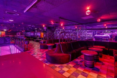 Intérieur d'une discothèque avec éclairage violet, escalier central, balustrades métalliques et sol carrelé coloré.
