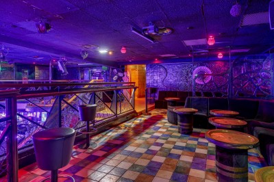 Intérieur d'une discothèque avec éclairage violet, escalier central, balustrades métalliques et sol carrelé coloré.