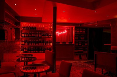 Salle intimiste éclairée par une lumière rouge, avec banquettes, petites tables rondes et rideaux sombres.