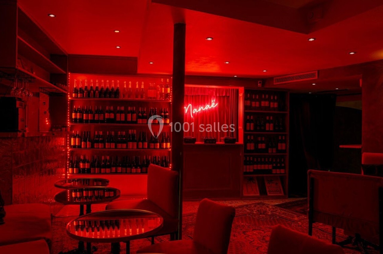 Salle de bar à l'éclairage rouge tamisé, avec des étagères remplies de bouteilles et un néon lumineux au mur.