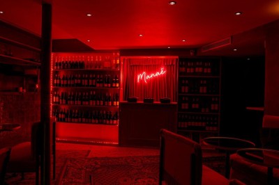 Salle intimiste éclairée par une lumière rouge, avec banquettes, petites tables rondes et rideaux sombres.