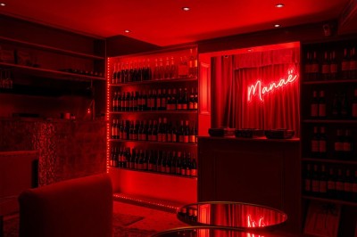 Salle intimiste éclairée par une lumière rouge, avec banquettes, petites tables rondes et rideaux sombres.