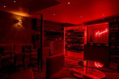 Salle intimiste éclairée par une lumière rouge, avec banquettes, petites tables rondes et rideaux sombres.