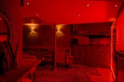 Salle intimiste éclairée par une lumière rouge, avec banquettes, petites tables rondes et rideaux sombres.