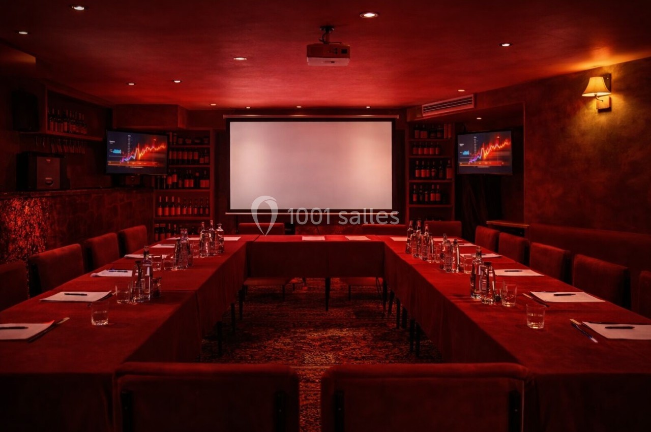 Salle de réunion sombre avec éclairage rouge, écran de projection central et tables disposées en U avec documents et…