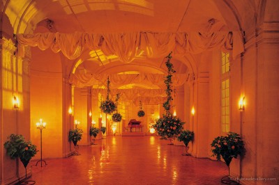 Salle lumineuse avec grandes baies vitrées, tables rondes en métal et lustres suspendus sous un plafond décoré.