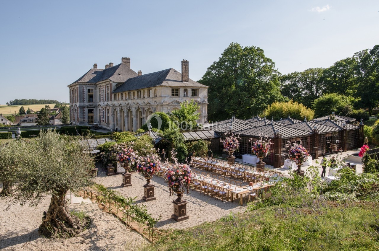 Tables décorées pour un événement en plein air devant un château entouré de jardins et de verdure.