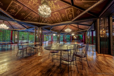 Salle lumineuse avec grandes baies vitrées, tables rondes en métal et lustres suspendus sous un plafond décoré.