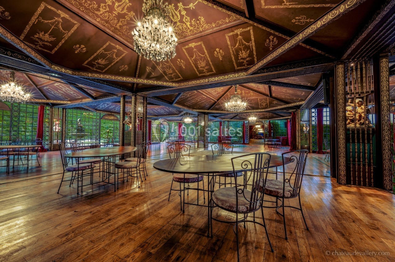 Salle spacieuse avec parquet en bois, tables et chaises en fer forgé, lustres suspendus et décorations murales élégantes.