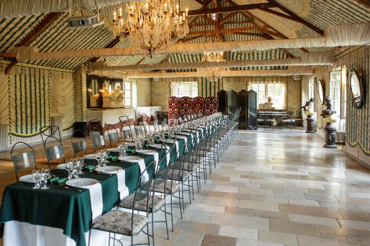 Salle de réception élégante avec longues tables dressées, nappes vertes et blanches, lustres et décoration raffinée.