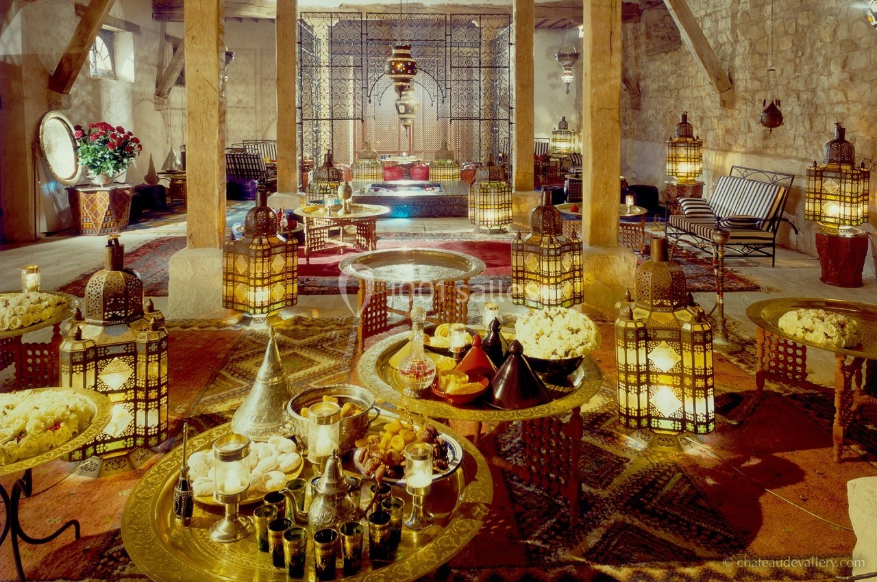 Salle décorée dans un style oriental avec tables basses en métal, lanternes, tapis et coussins colorés.
