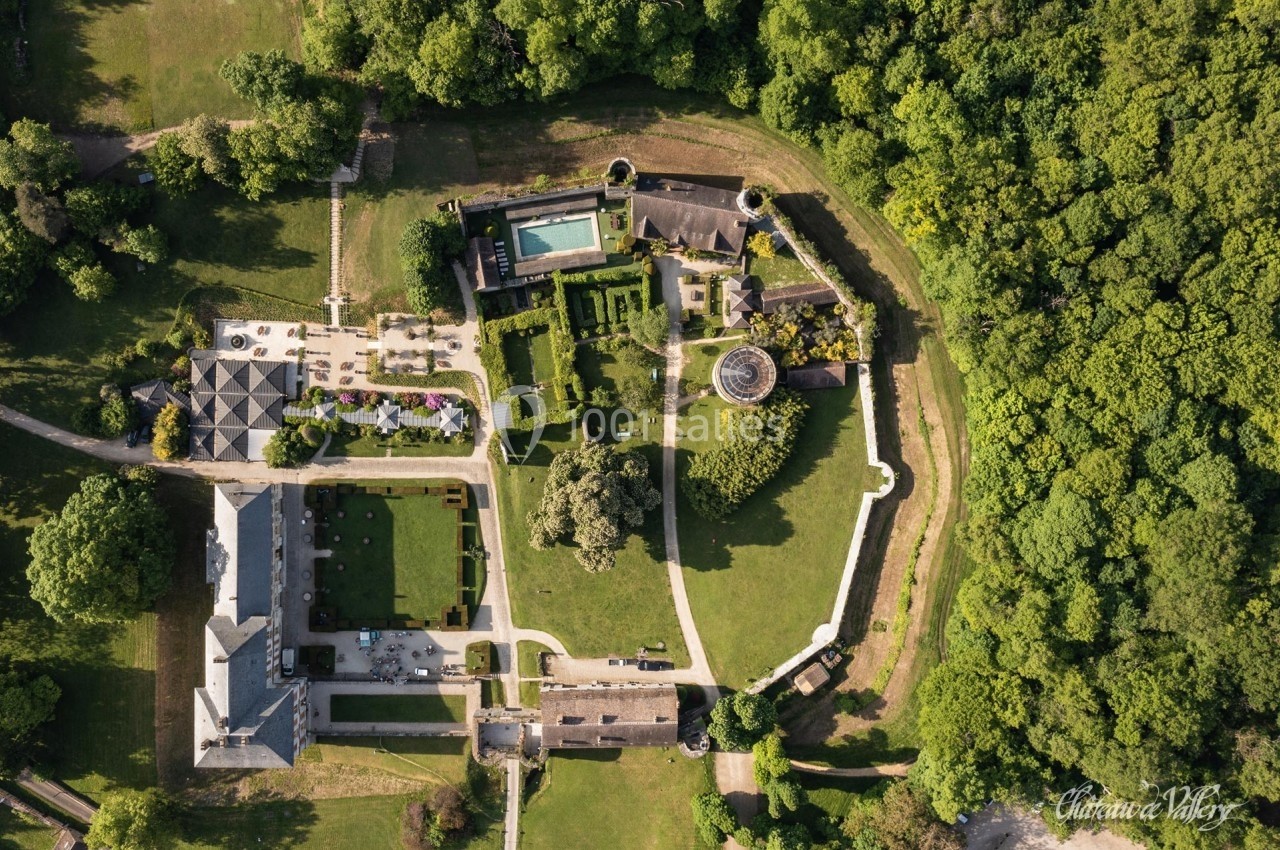 Vue aérienne d'un domaine avec jardins, bâtiments, piscine et espaces verts entourés de forêt dense.