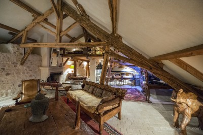 Salle lumineuse avec grandes baies vitrées, tables rondes en métal et lustres suspendus sous un plafond décoré.