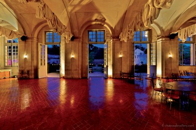 Salle lumineuse avec grandes baies vitrées, tables rondes en métal et lustres suspendus sous un plafond décoré.