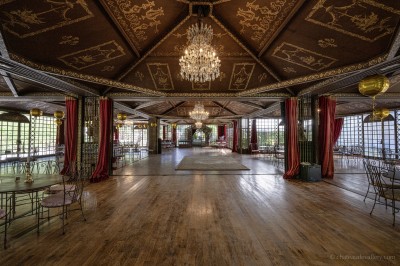 Salle lumineuse avec grandes baies vitrées, tables rondes en métal et lustres suspendus sous un plafond décoré.