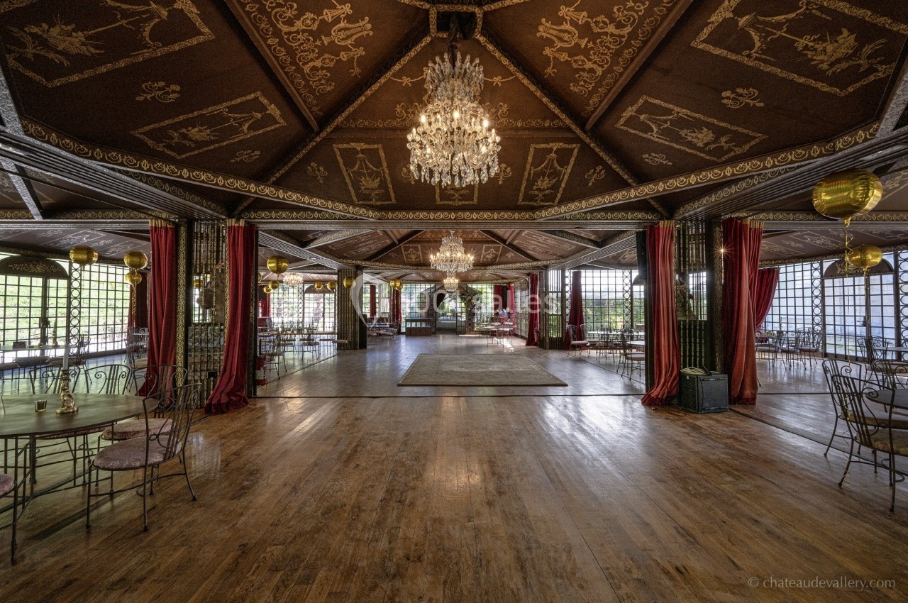 Salle de réception spacieuse avec parquet en bois, lustres, plafonds ornés et grandes baies vitrées entourées de rideaux…