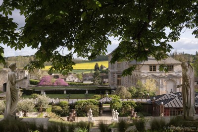 Salle lumineuse avec grandes baies vitrées, tables rondes en métal et lustres suspendus sous un plafond décoré.