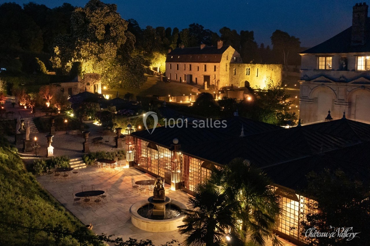 Vue nocturne d'un domaine illuminé avec bâtiments historiques, jardin aménagé et fontaine centrale.