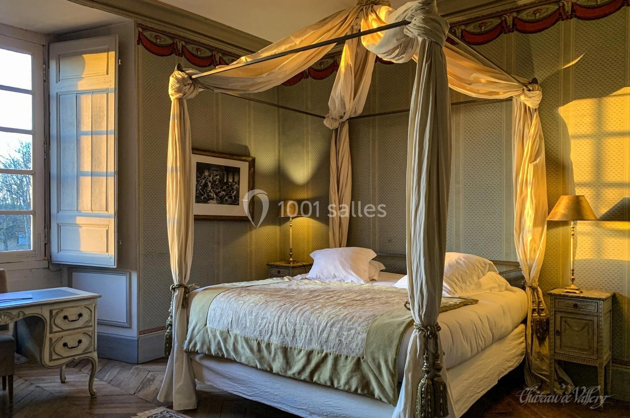 Lit à baldaquin dans une chambre élégante avec lumière naturelle, murs texturés et mobilier classique.