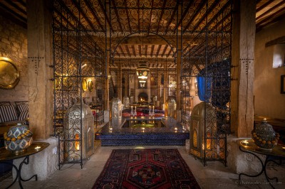 Salle lumineuse avec grandes baies vitrées, tables rondes en métal et lustres suspendus sous un plafond décoré.