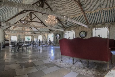 Salle lumineuse avec grandes baies vitrées, tables rondes en métal et lustres suspendus sous un plafond décoré.