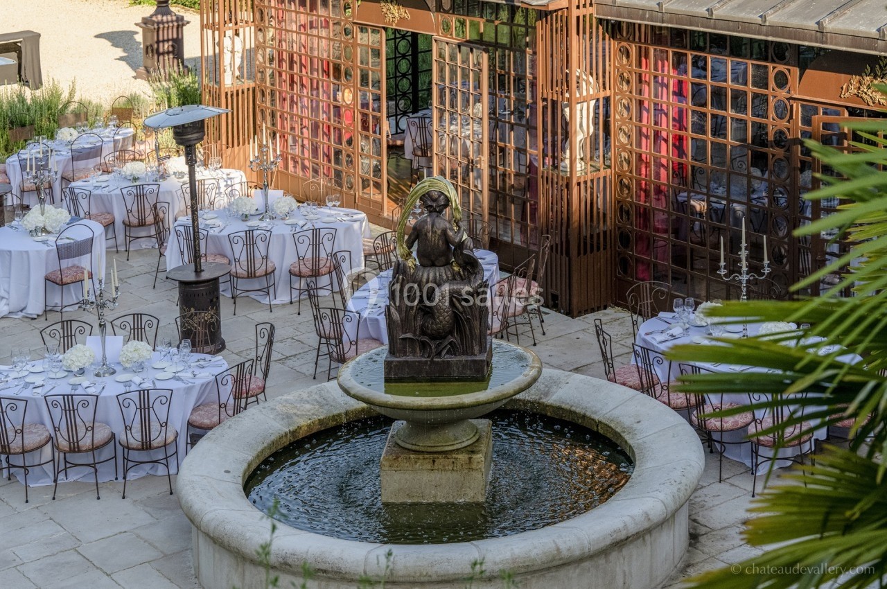 Fontaine centrale entourée de tables dressées pour un événement en extérieur, avec une façade vitrée en arrière-plan.