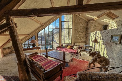 Salle lumineuse avec grandes baies vitrées, tables rondes en métal et lustres suspendus sous un plafond décoré.