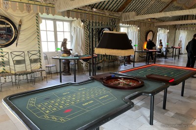 Salle lumineuse avec grandes baies vitrées, tables rondes en métal et lustres suspendus sous un plafond décoré.