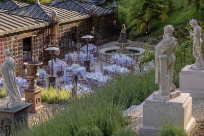 Salle lumineuse avec grandes baies vitrées, tables rondes en métal et lustres suspendus sous un plafond décoré.