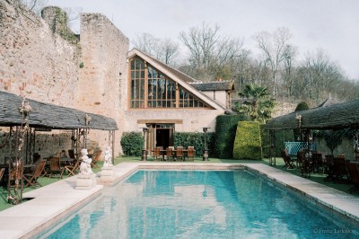 Salle lumineuse avec grandes baies vitrées, tables rondes en métal et lustres suspendus sous un plafond décoré.
