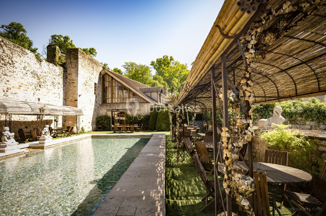 Piscine extérieure bordée de murs en pierre, terrasse ombragée avec mobilier en bois et végétation environnante.