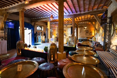 Salle lumineuse avec grandes baies vitrées, tables rondes en métal et lustres suspendus sous un plafond décoré.