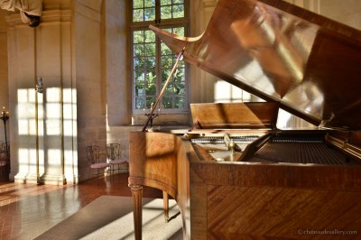 Salle lumineuse avec grandes baies vitrées, tables rondes en métal et lustres suspendus sous un plafond décoré.