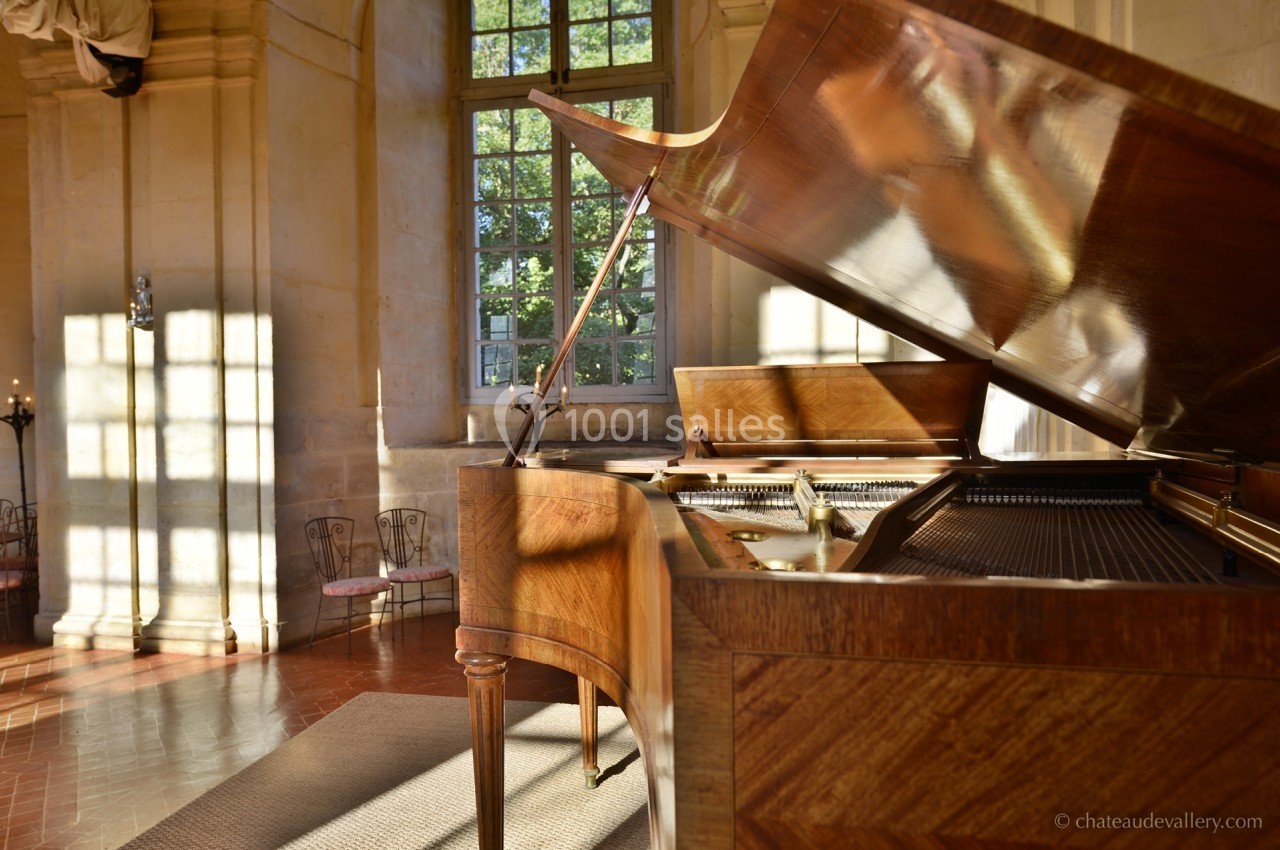 Piano à queue en bois dans une pièce lumineuse avec de grandes fenêtres et des murs en pierre.