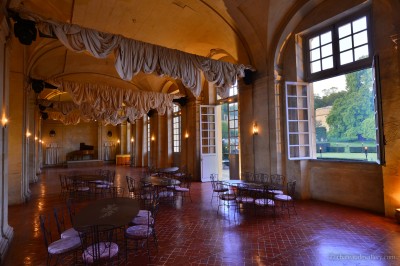 Salle lumineuse avec grandes baies vitrées, tables rondes en métal et lustres suspendus sous un plafond décoré.