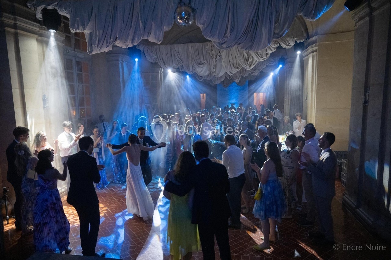 Groupe de personnes dans une salle éclairée par des lumières colorées, dansant et socialisant lors d'un événement festif.