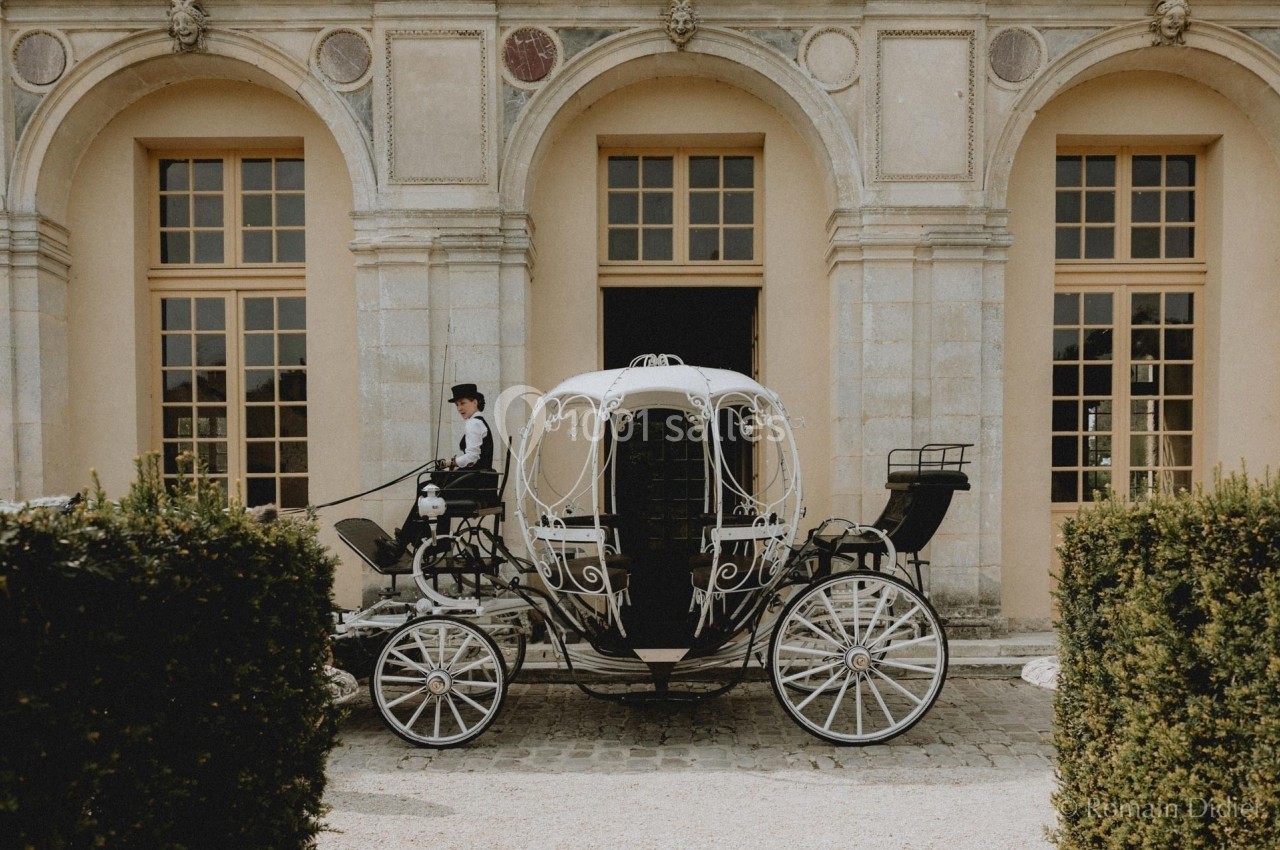 Calèche élégante noire et blanche stationnée devant un bâtiment ancien avec fenêtres à croisillons.