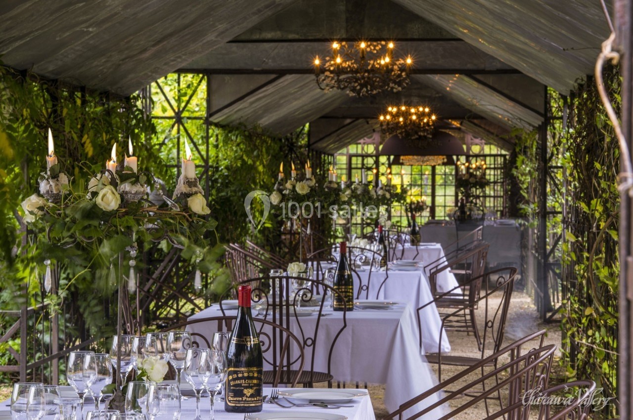 Salle à manger en plein air sous une pergola, avec tables dressées et décorations florales élégantes.