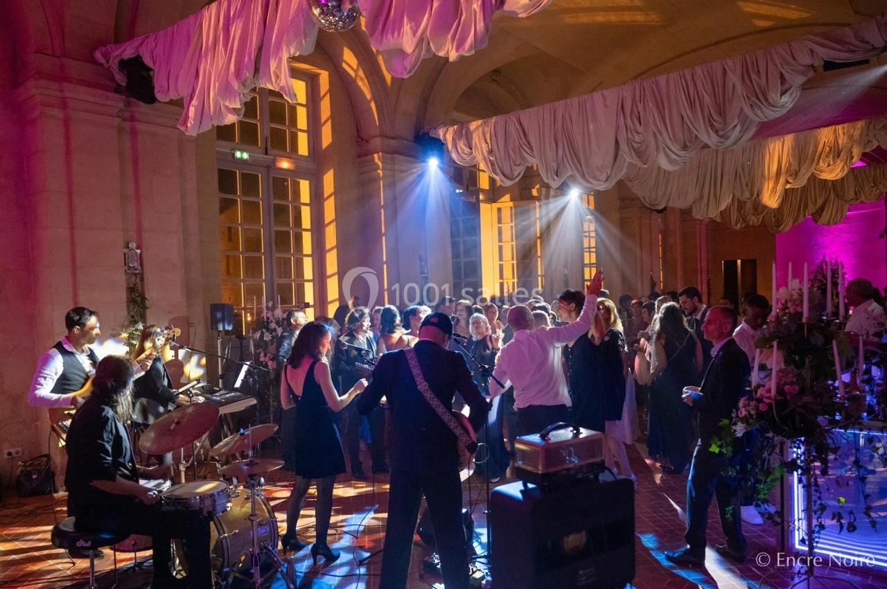 Groupe de musiciens jouant devant une foule dans une salle éclairée par des lumières colorées et décorée de tentures.