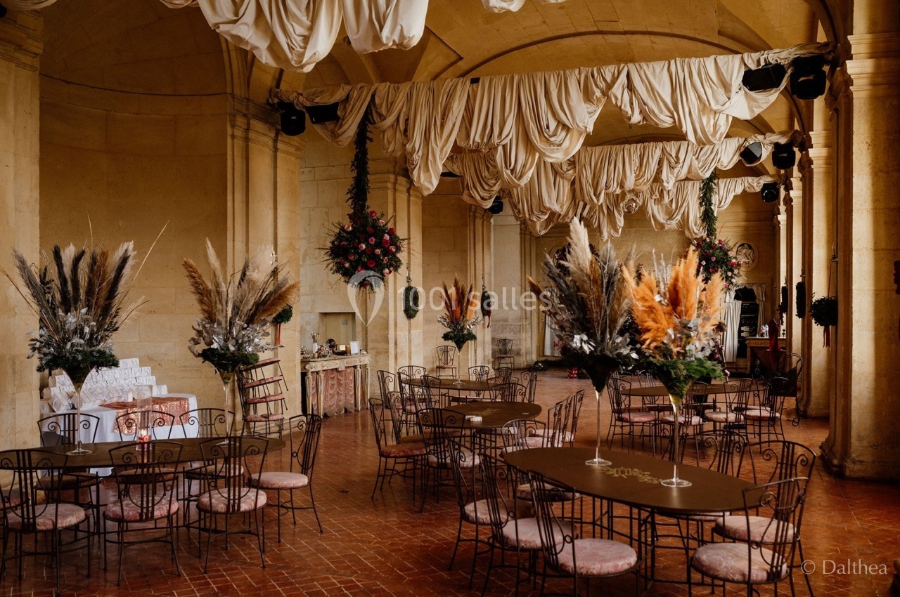 Salle de réception avec tables en fer forgé, décorations florales séchées et drapés suspendus au plafond.