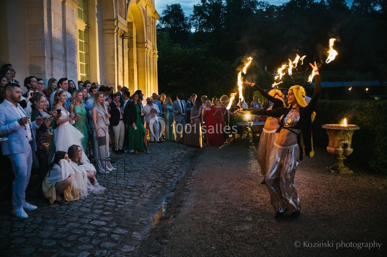 Danseuses manipulant des torches enflammées devant un public rassemblé près d'un bâtiment éclairé en soirée.
