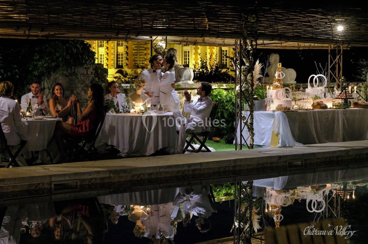 Des invités dînent en extérieur près d'une piscine, avec une table de desserts décorée en arrière-plan.