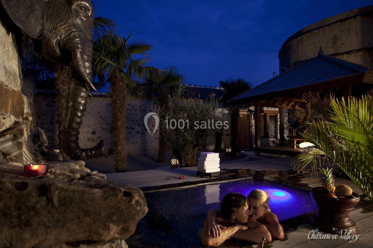 Un couple se détend dans un bassin extérieur éclairé, entouré de palmiers et d'une statue d'éléphant.