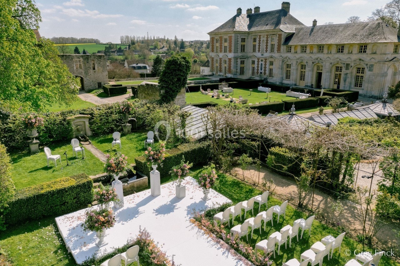 Cérémonie de mariage en plein air avec une allée décorée de fleurs, dans le jardin d'un château historique.
