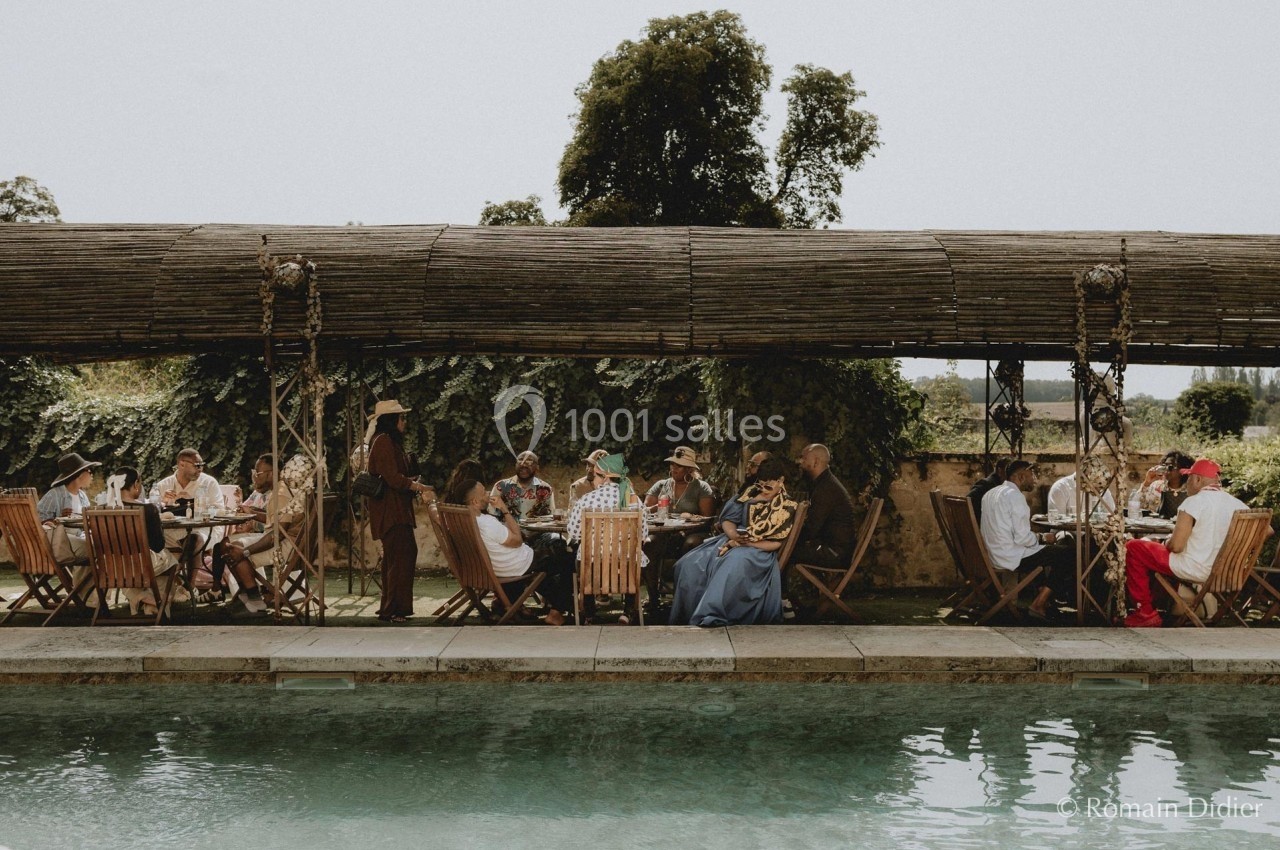 Groupe de personnes assises autour d'une table en plein air près d'une piscine, sous une pergola en bois.