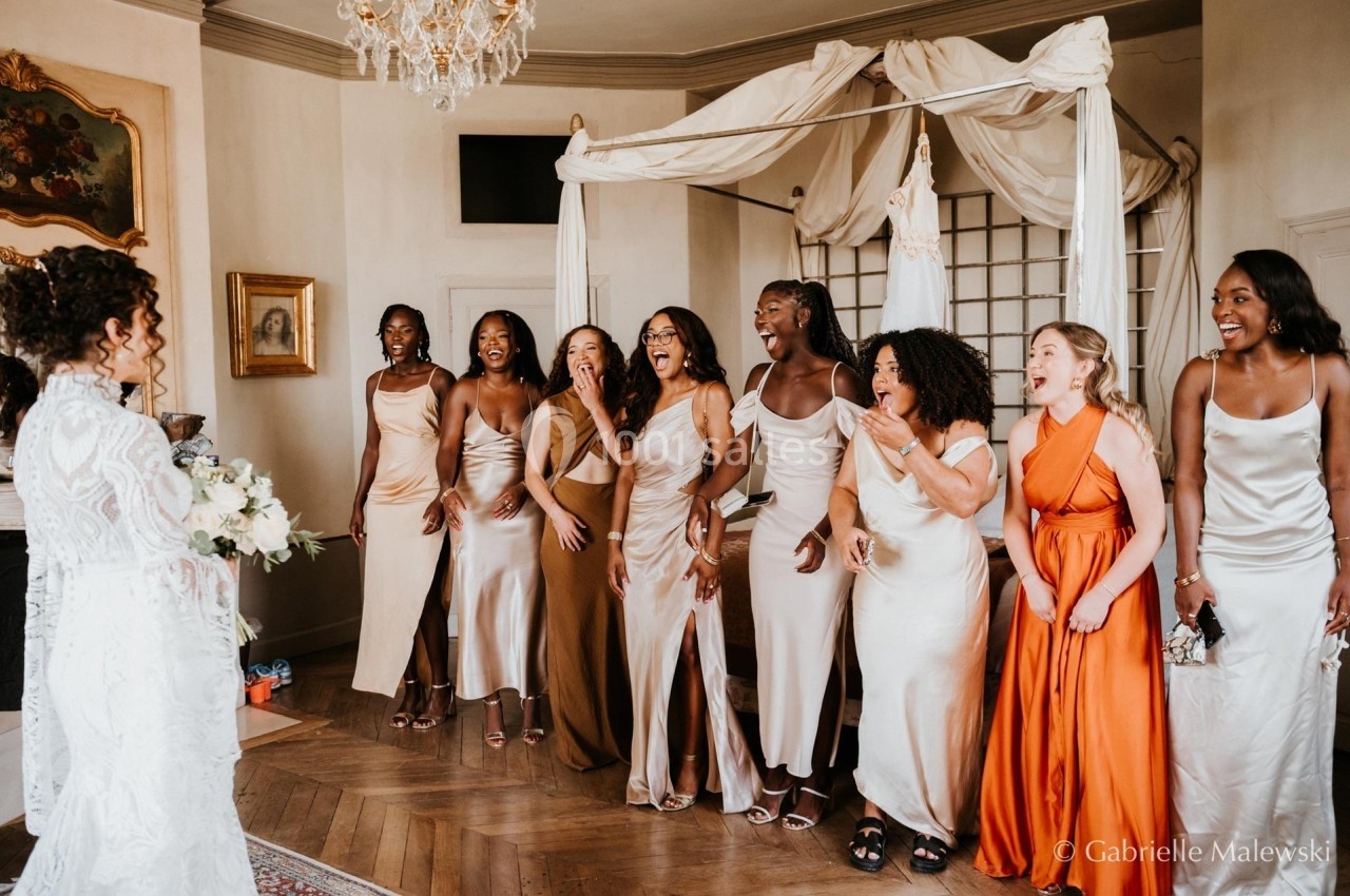 Un groupe de femmes en robes élégantes réagit avec joie face à une mariée dans une pièce décorée.