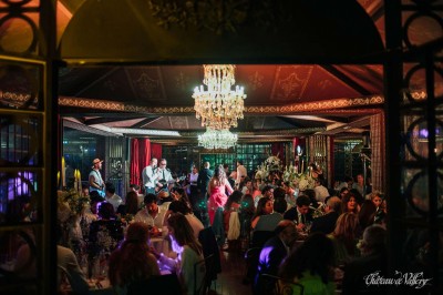 Un groupe de femmes en robes élégantes réagit avec joie face à une mariée dans une pièce décorée.