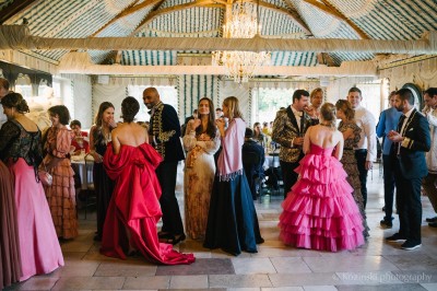 Un groupe de femmes en robes élégantes réagit avec joie face à une mariée dans une pièce décorée.